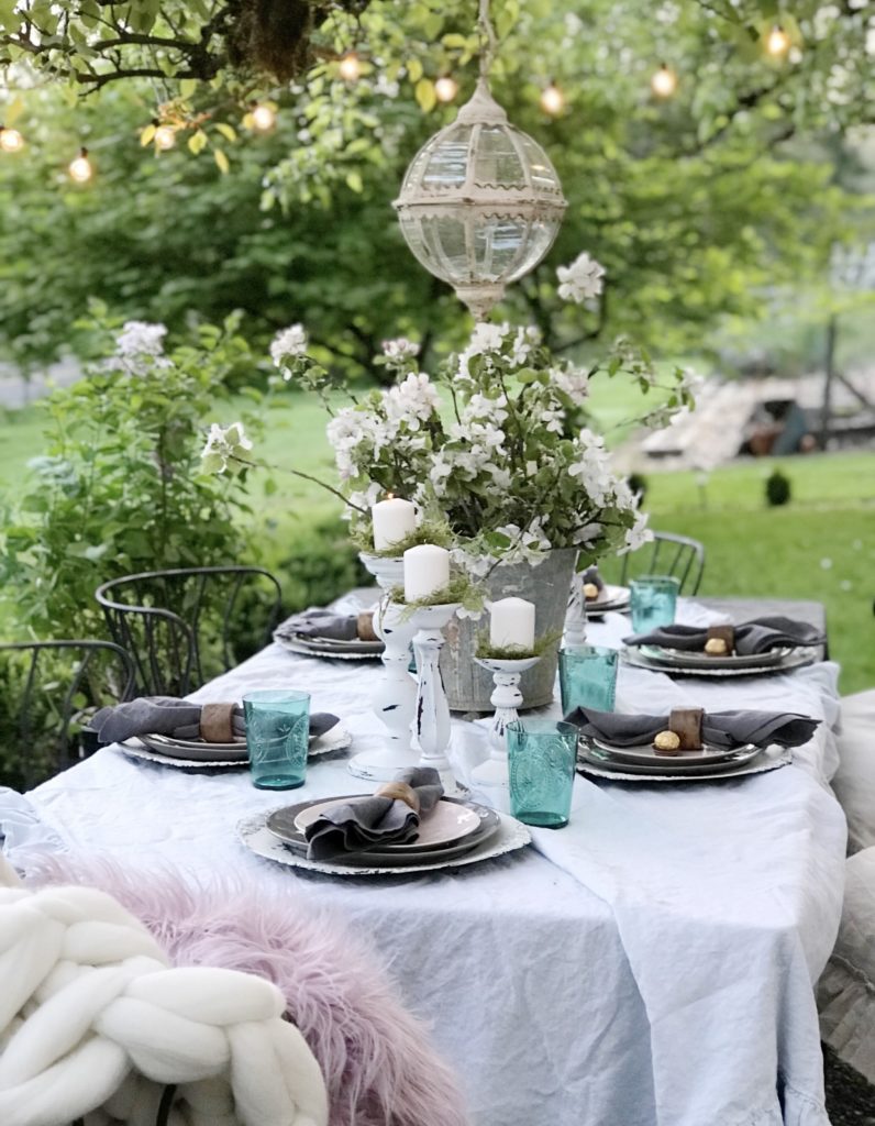 ruffle linen table cloth with 6 white candle holders and blue cups silver bucket with white flowers and round glass chandeleier