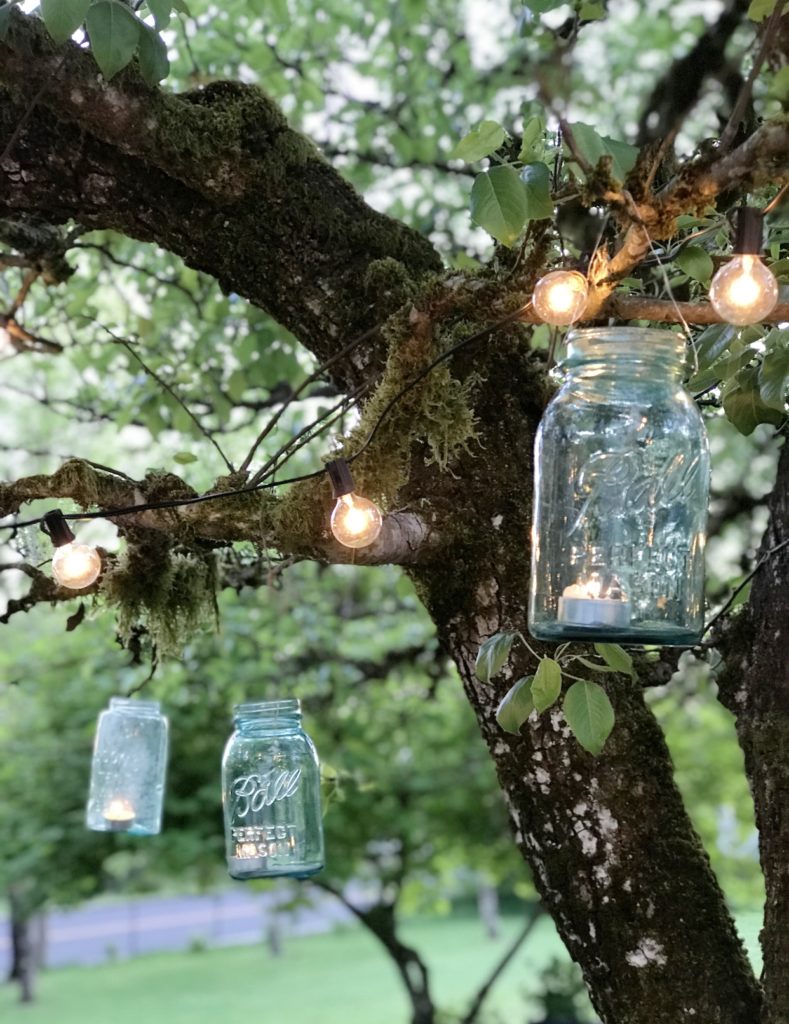 3 blue mason jars hanging from tree with lights