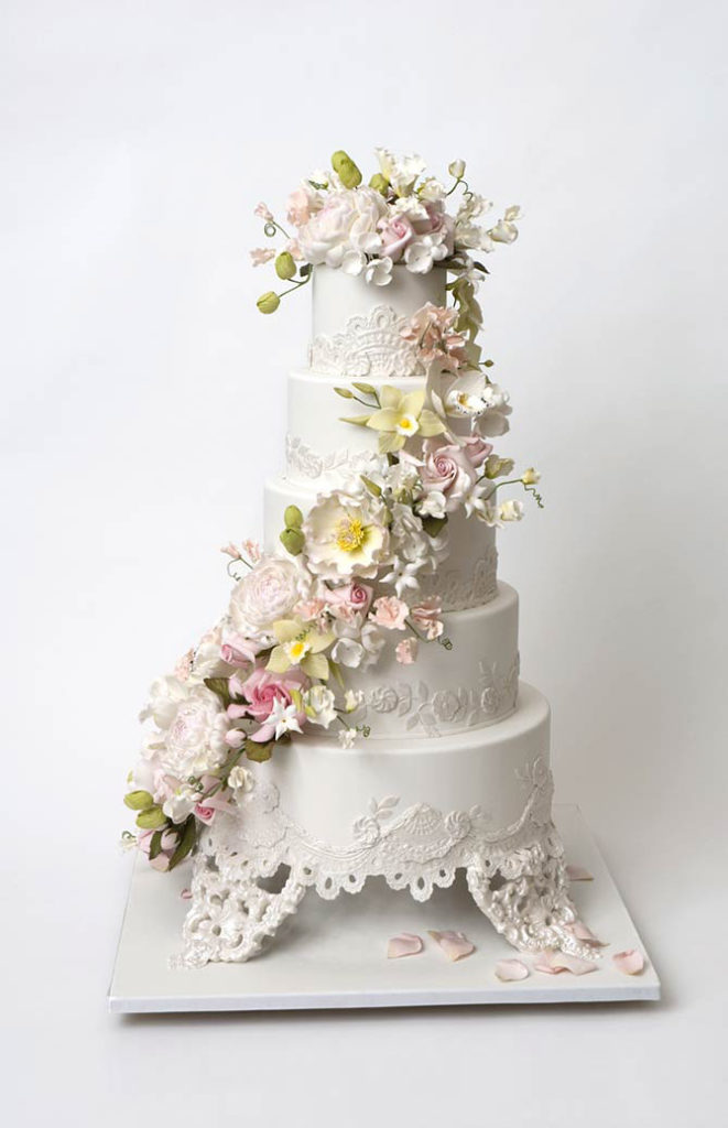 white lace 5 tier cake with yellow and pink flowers wrapping around it