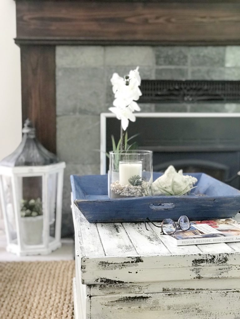 Blue Chalk Painted Farmhouse Tray on white chippy painted trunk with clear candle and book with glasses