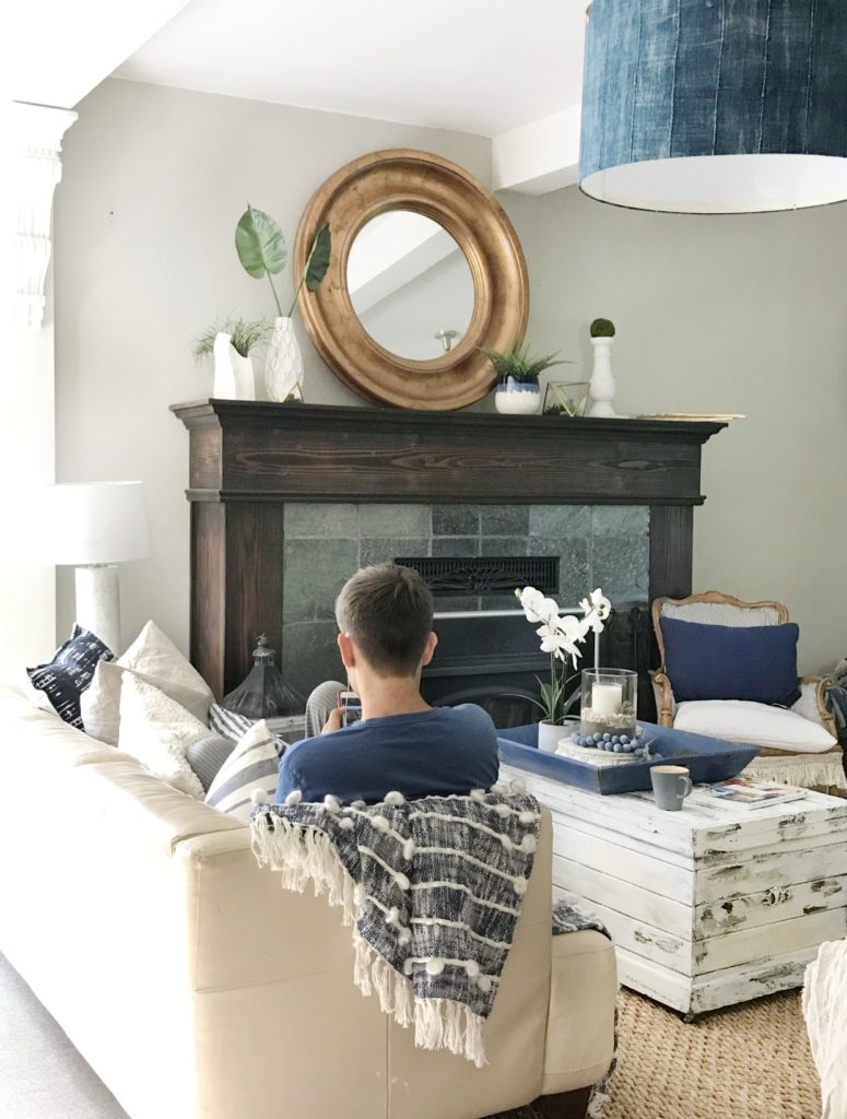 How To Make Relaxed Easy Farmhouse Style Home with Kids one on couch. fire place mantle with round gold mirror and round blue light 