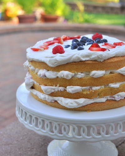 4 layer cake with white frosting and blueberries and strawberries on top