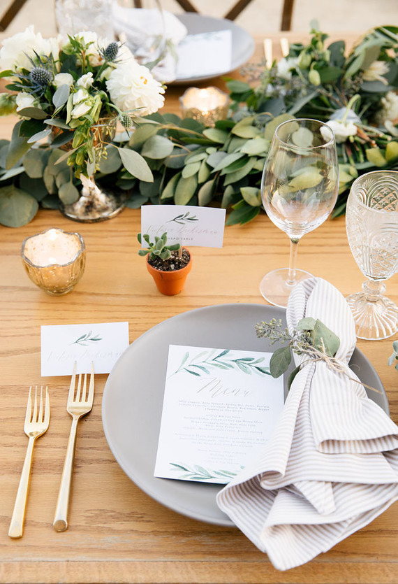 gray plate with gold silverware and greenery centerpiece