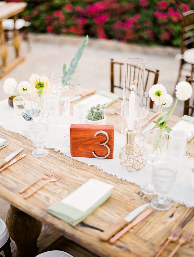 wood table with copper silverware and white table runner with clear glass vases and cups