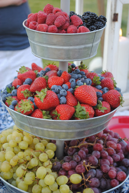 3 tier metal tray with raspberries and black berries ontop, strawberries and blueberries in middle and grapes on the bottom