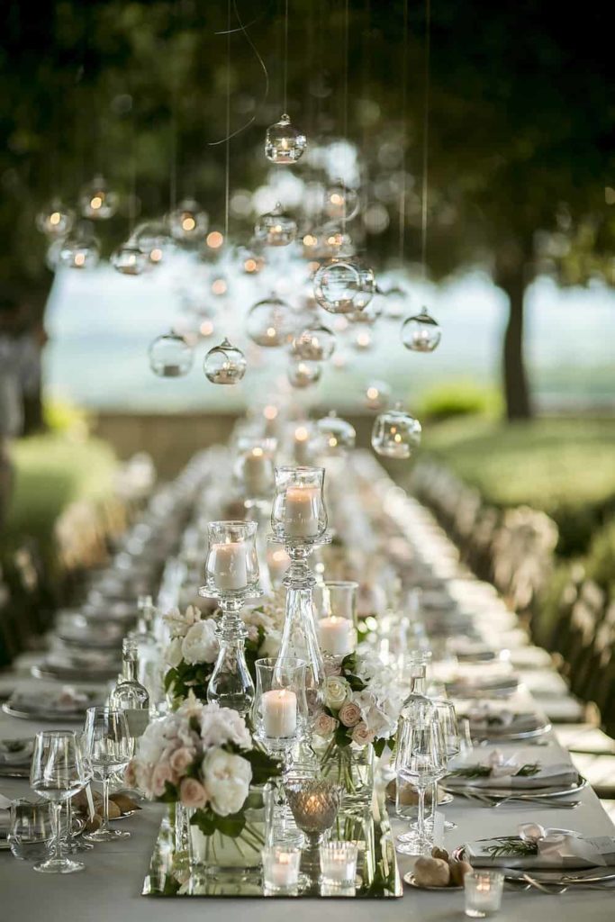 long wedding table with glass candle holder through out the whole table and hanging circle clear glass tea candle light holders