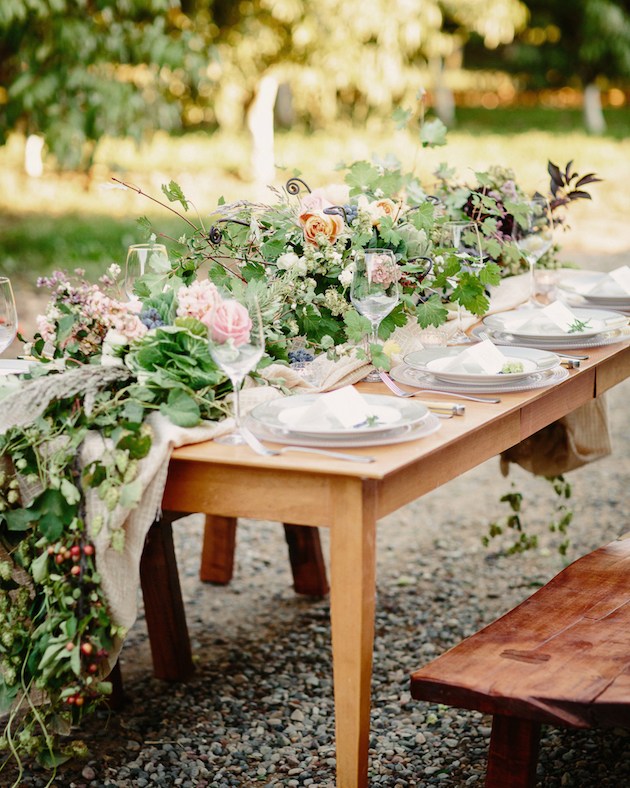 wood table with lots of greenery and pink and orange flowers running table white setting of 8 white plates