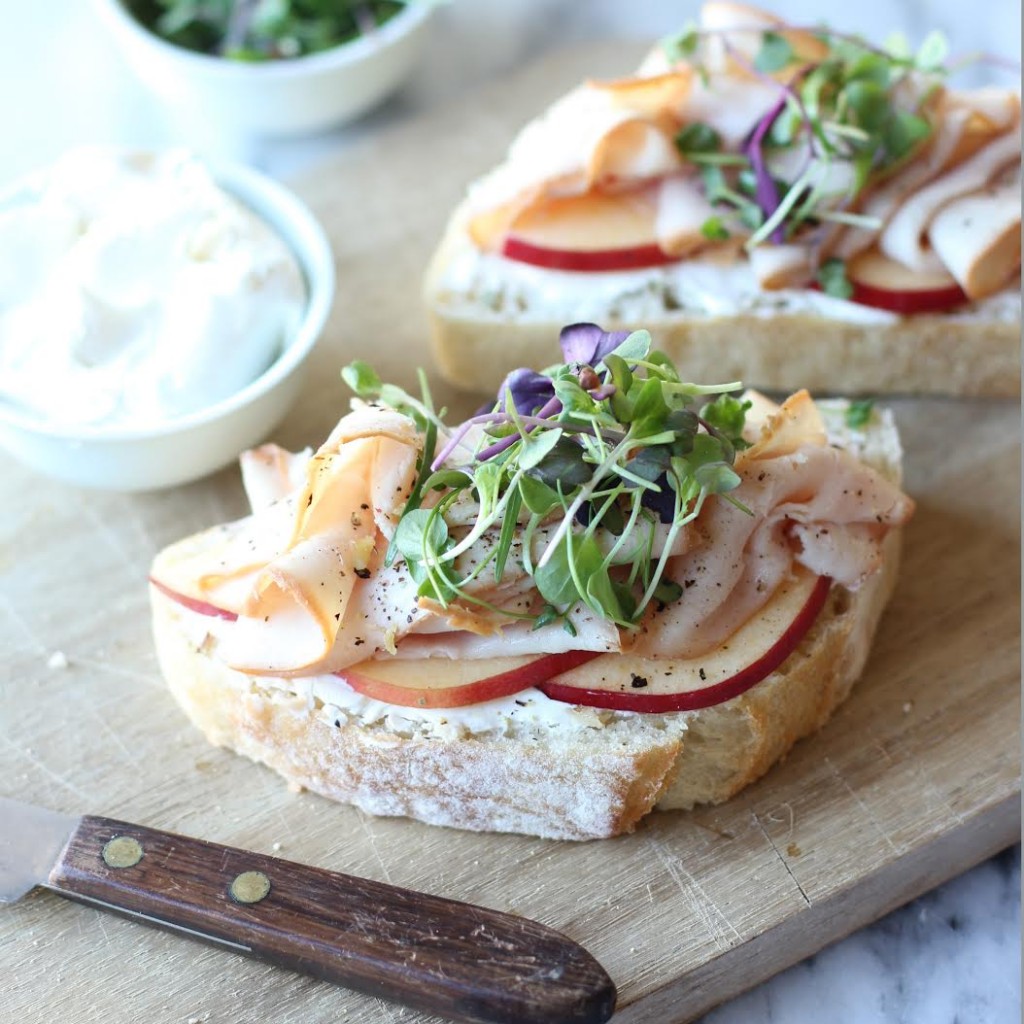 2 open faced sandwiches with apples turkey and sprouts on wood cutting board