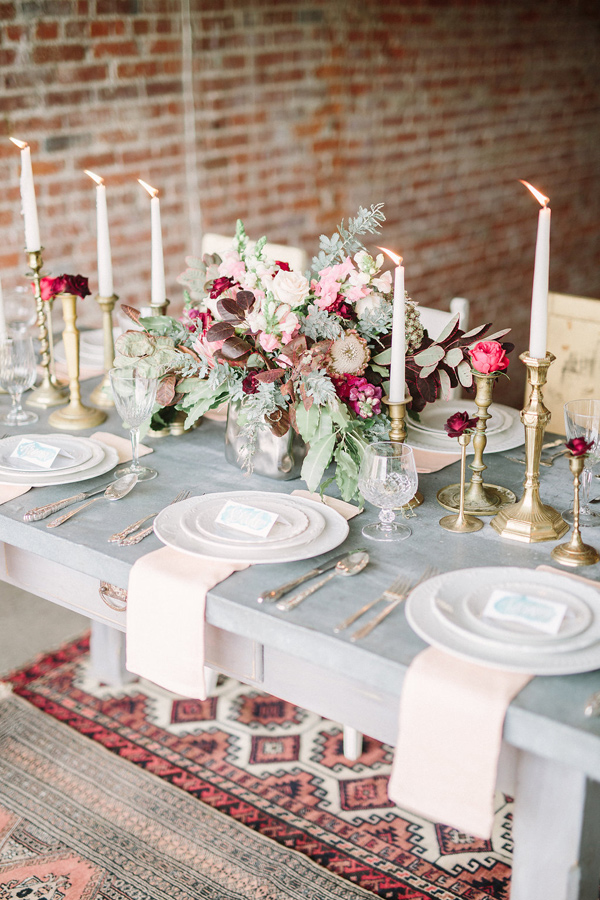 gray table with 6 white plate settings and gold candle holderswith red and pink flowers in the center