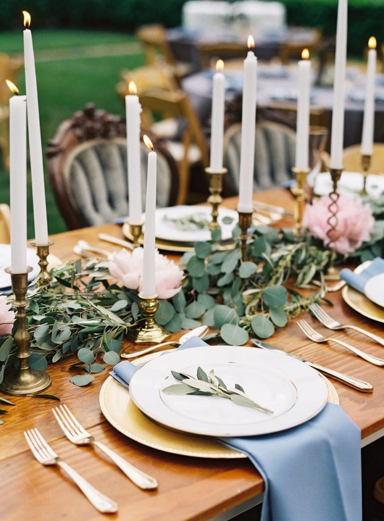 wedding table with gold and white plates with greenery in middle and cold candle holders