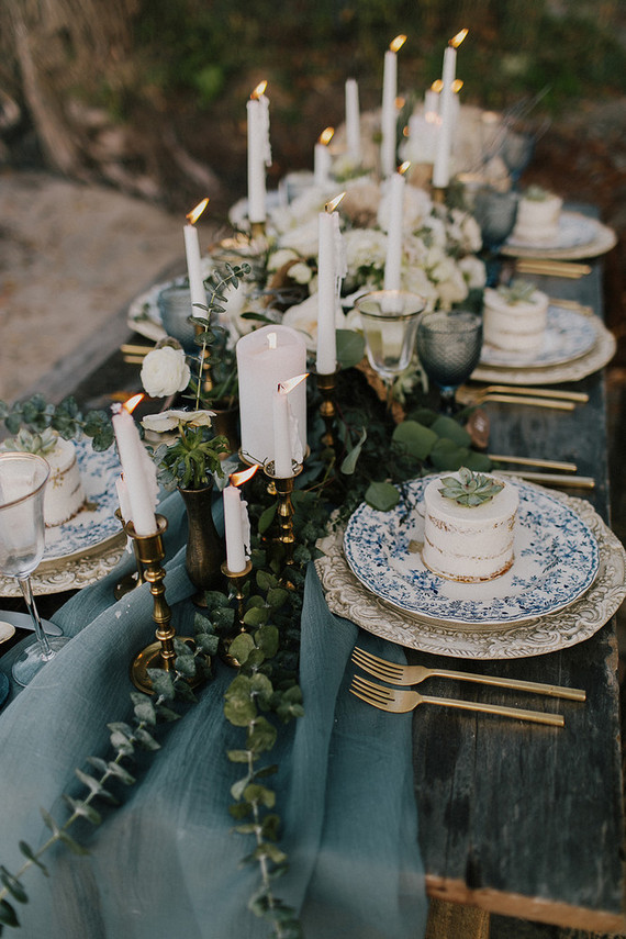 wood table white blue table runner and 6 blue plate with many gold candles in the middle 