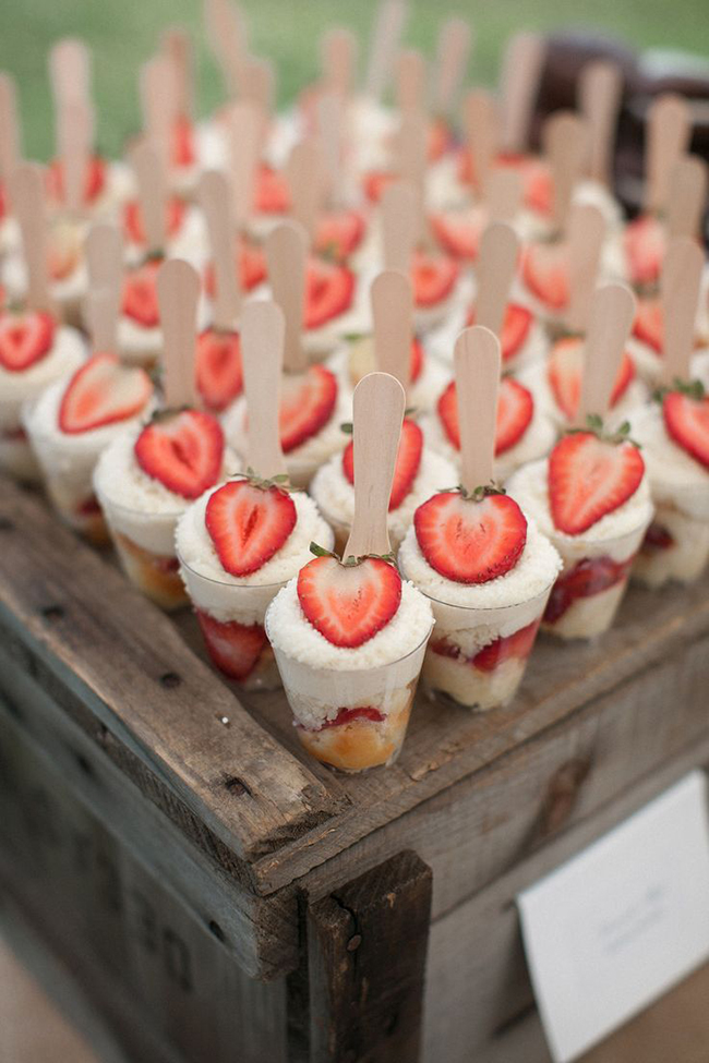 wood tray with many cups of strawberry short cakes with wooden spoons sticking out