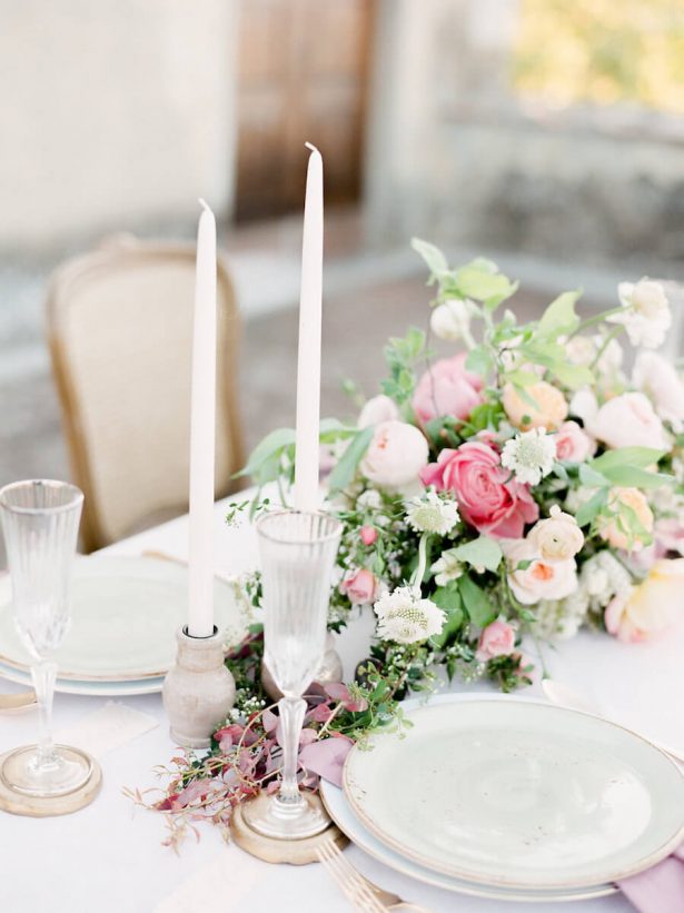 pink and green flower centerpeice with tall white candles and white plates with gold edge