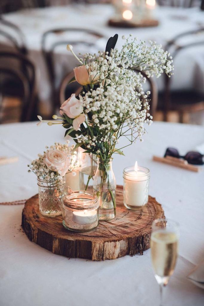 log round centerpiece with jar candles and vase of baby breath and roses
