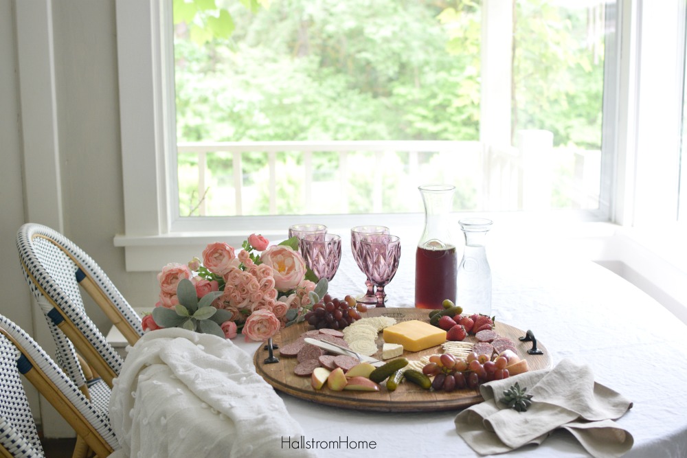 cheese platter on table with cups and bouquet of pink flowers