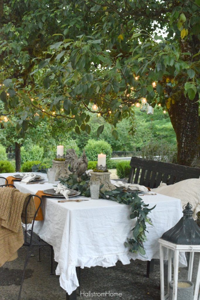 Celebrate Autumn with the Most Perfect Tablescape with orange sweater on chair and rooster and 2 candle pedestals as centerpiece with greenery down middle