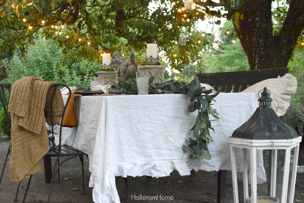 Celebrate Autumn with the Most Perfect Tablescape with orange sweater on chair and rooster and 2 candle pedestals as centerpiece with greenery down middle