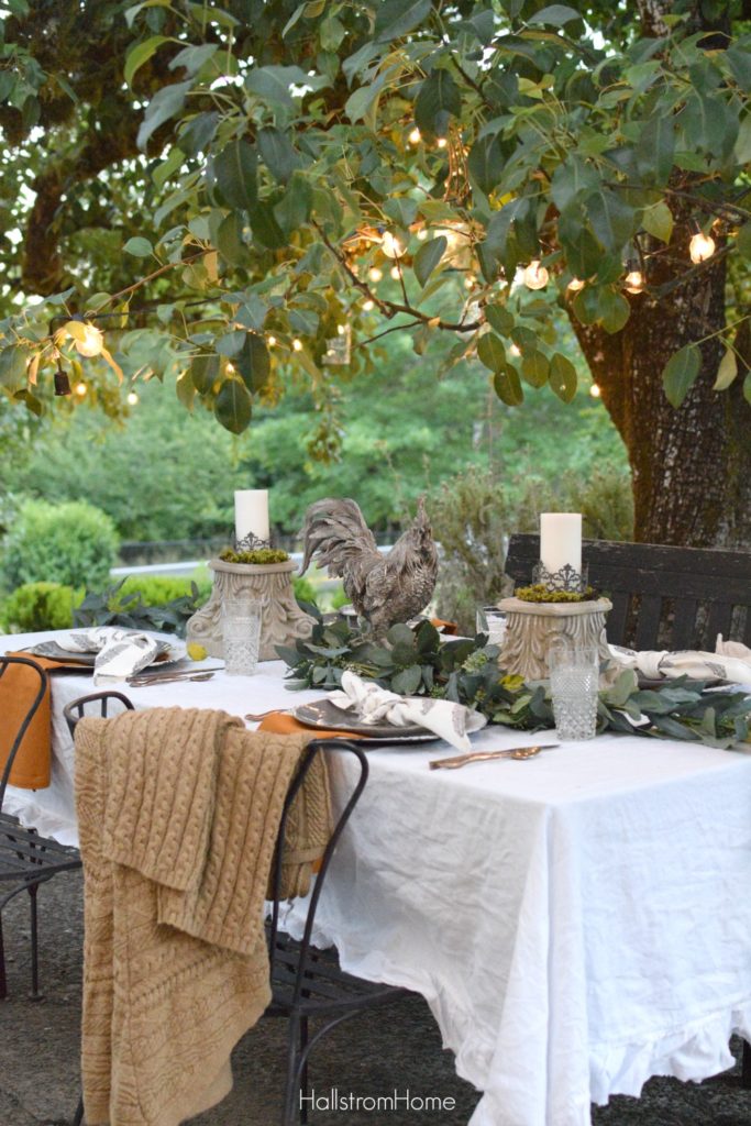 Celebrate Autumn with the Most Perfect Tablescape with orange sweater on chair and rooster and 2 candle pedestals as centerpiece with greenery down middle