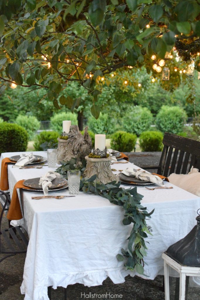 Celebrate Autumn with the Most Perfect Tablescape with orange sweater on chair and rooster and 2 candle pedestals as centerpiece with greenery down middle