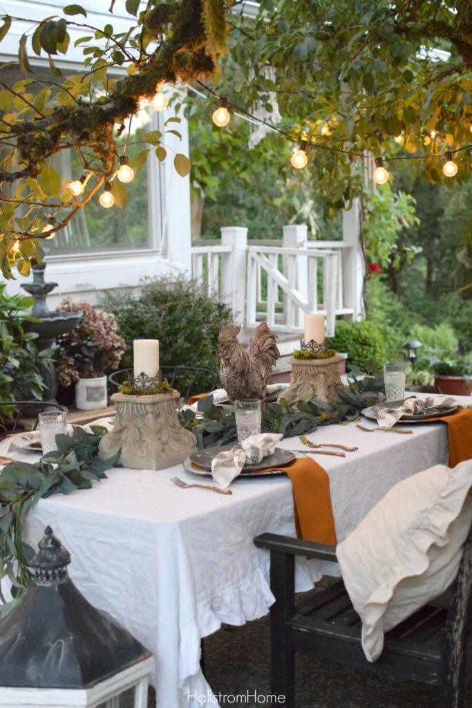 Celebrate Autumn with the Most Perfect Tablescape with orange sweater on chair and rooster and 2 candle pedestals as centerpiece with greenery down middle