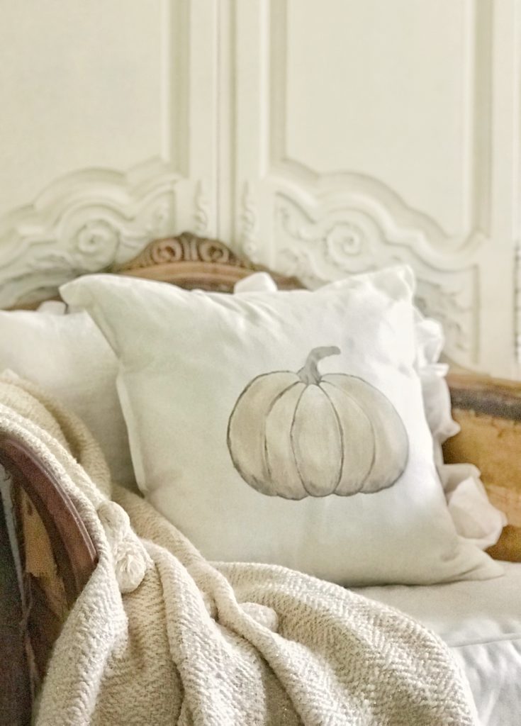 white pumpkin pillow on wooden chair with knit pom pom blanket