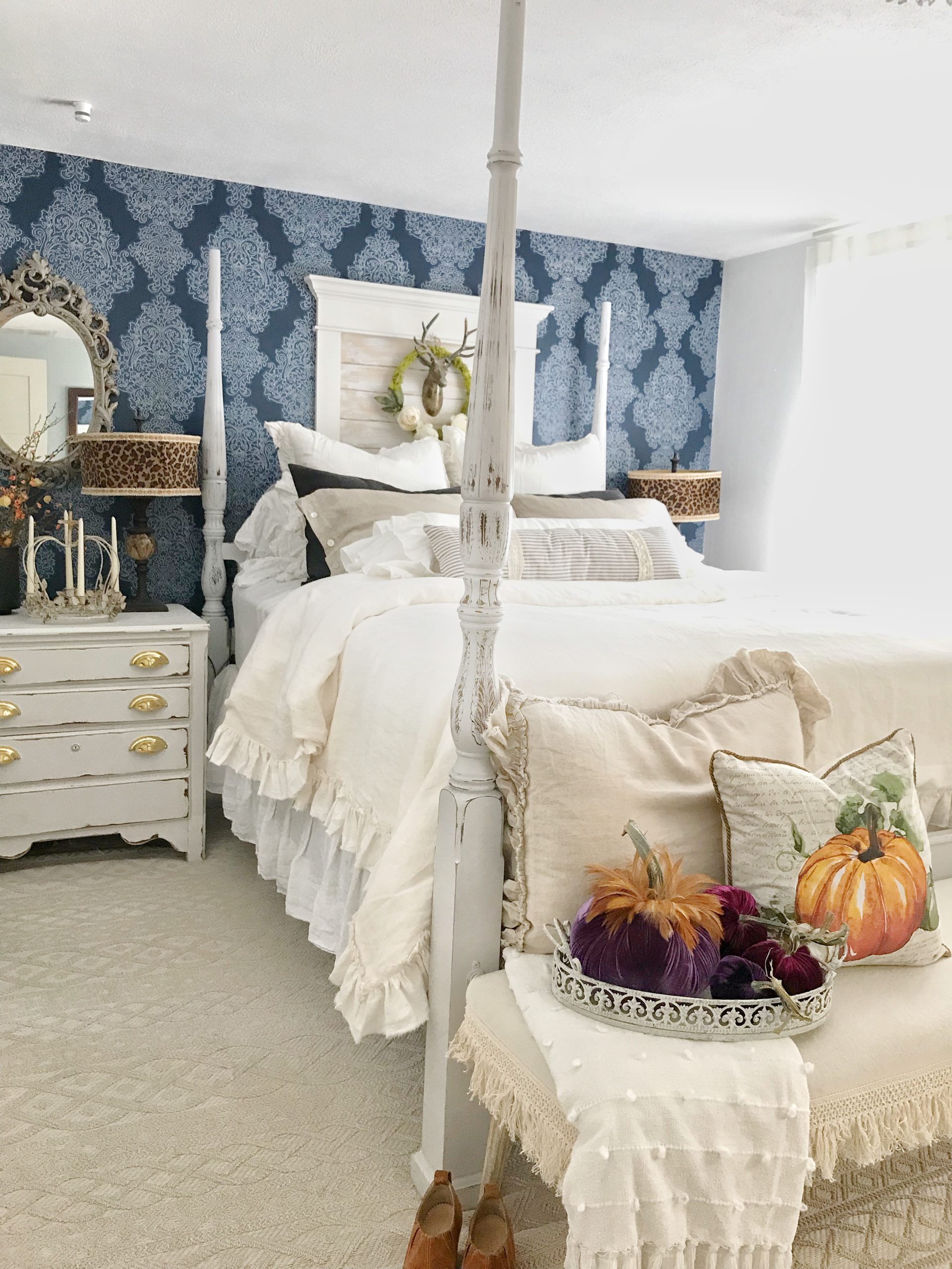 How to Decorate Bedrooms for Easy Fall Decor cream bedding with 8 pillows and velvet pumpkins on bench in front and pumpkin pillow