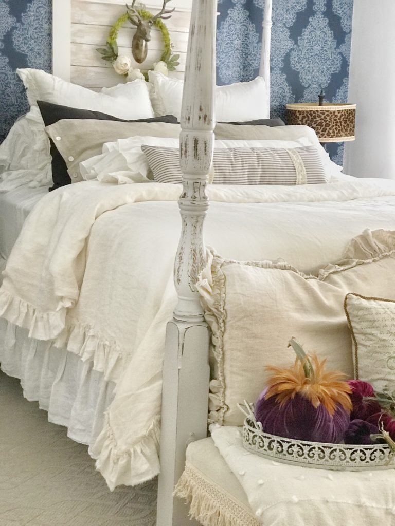 linen ruffle bed with purple velvet pumpkins on bench in front of bed