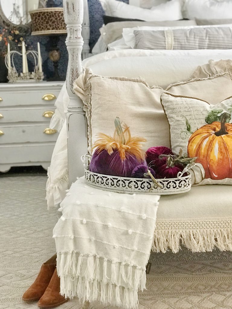 linen ruffle bed with purple velvet pumpkins on bench in front of bed