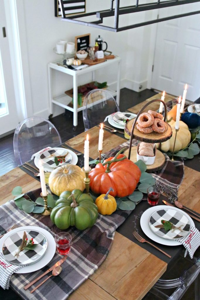 table with 3 large pumpkins plaid table runner and 6 candles