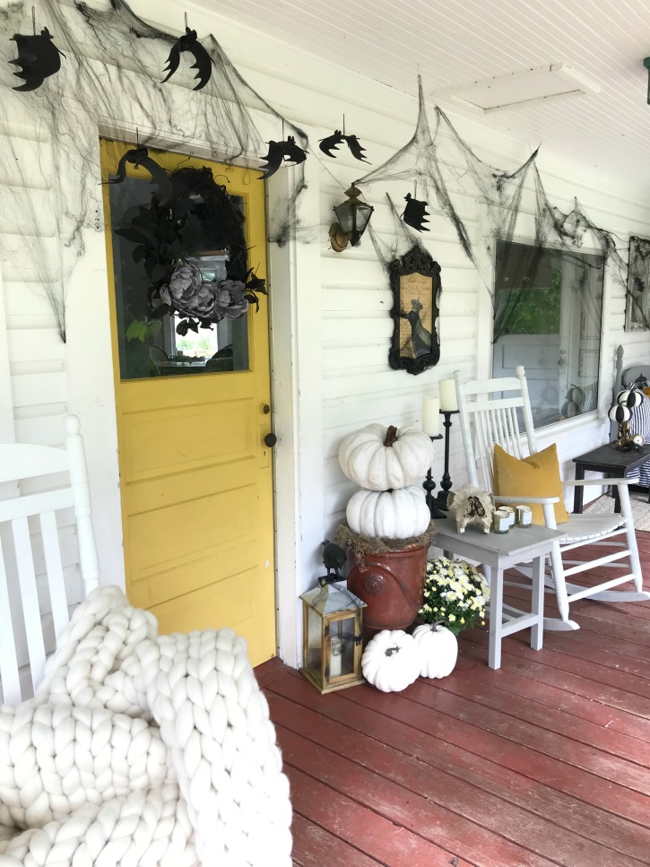 Simple, Easy Halloween Porch Decorating You Can Actually Do with yellow door and black wreath with white stack of pumpkins and bats hanging around