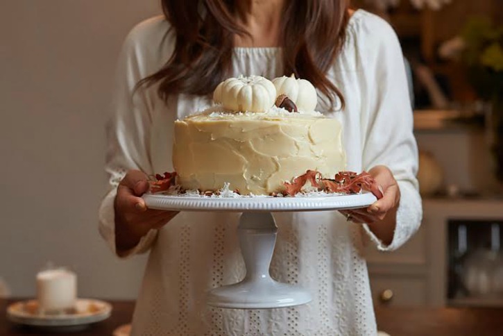 Happy Happy Nester Holding white pumpkin cake on white cake platter