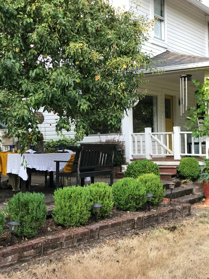 white farmhouse with 5 bushes and table outside