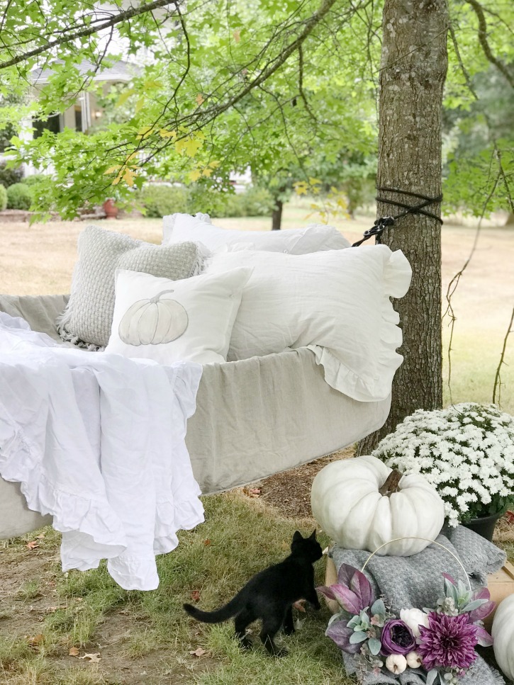 hammock filled with white linens and pumpkin pillow with pumpkins and mums on ground