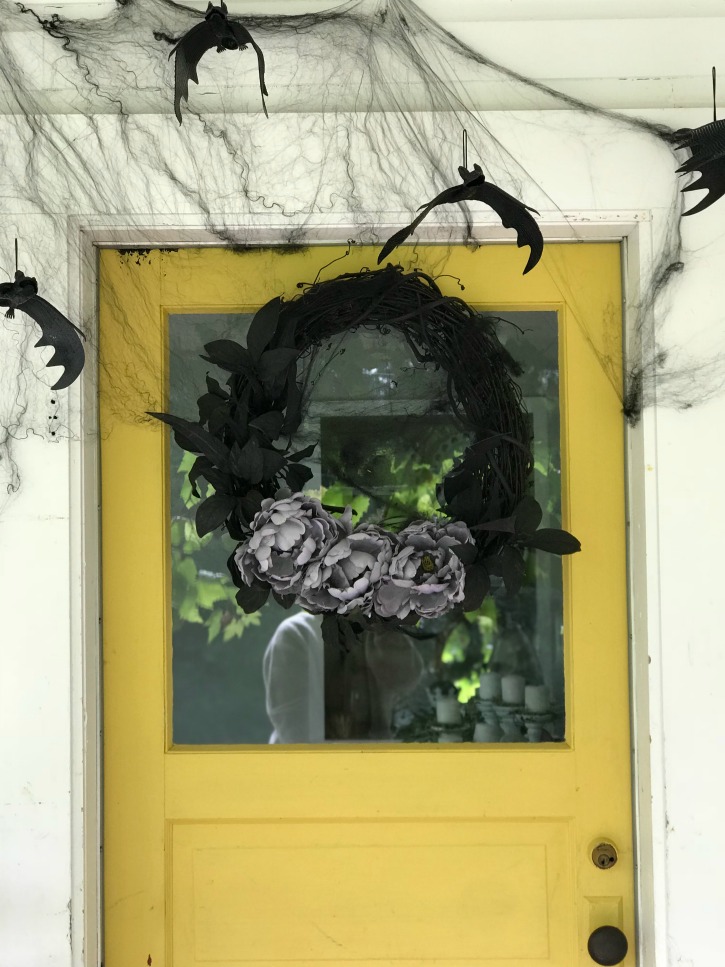 yellow door with black wreath and purple rose and cobwebs with bats