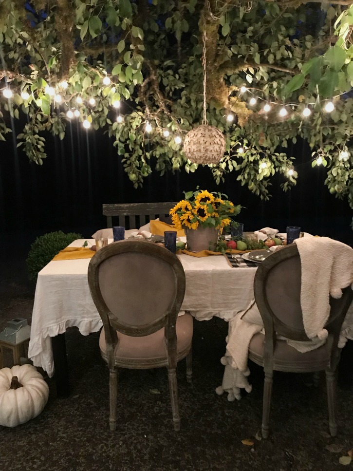 outdoor table with white linen tablecloth and bouquet of sunflowers with round chandelier